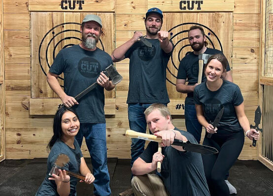 group of six posing for a photo with axes and throwing knives at an axe throwing bar